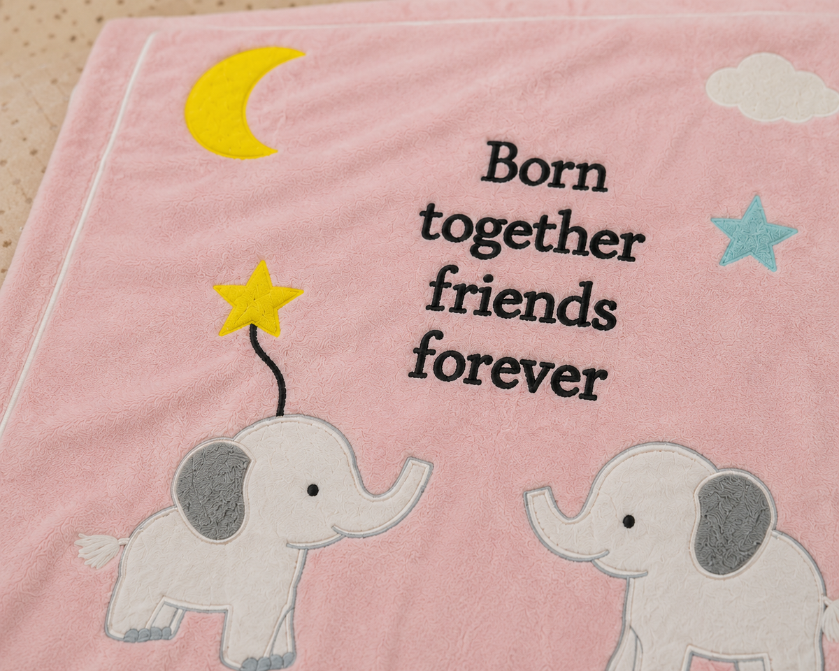 Close up of Born Together Friends Forever Twin Baby Blanket Pink Edition showing two white grey elephant appliques golden star balloon and mint stars on blush pink velvet