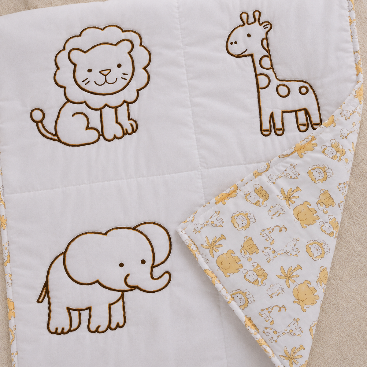 Close up of Little Safari Baby Blanket showing embroidered lion giraffe and elephant on white quilted fabric with reversible yellow safari print back